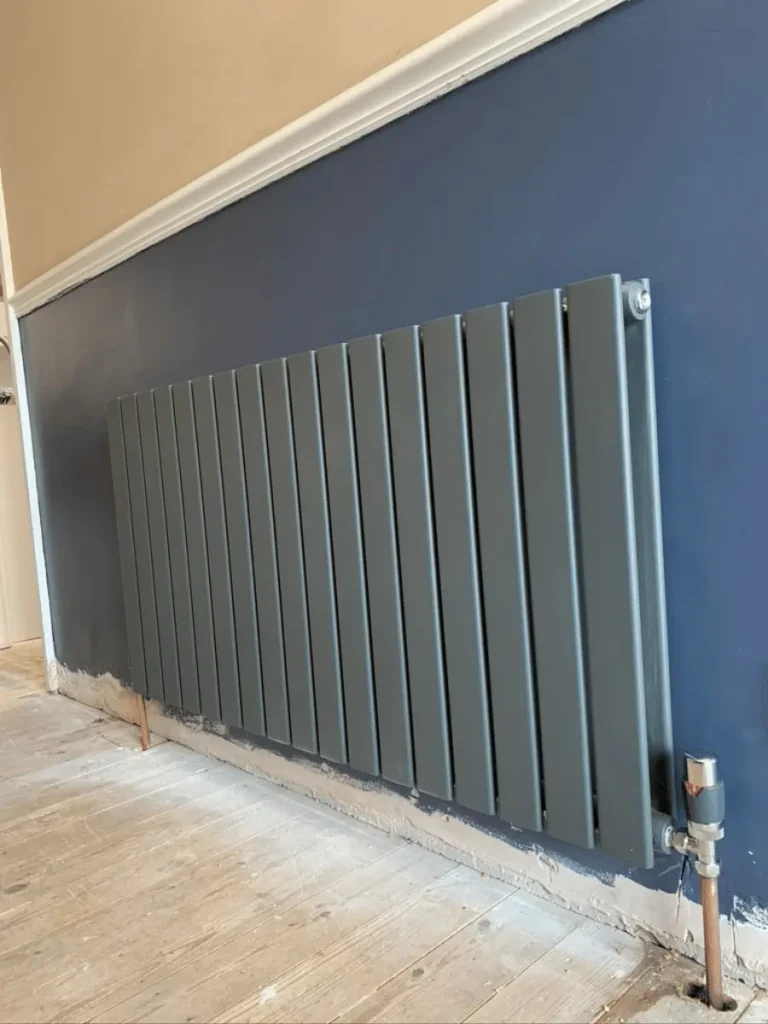 Modern anthracite horizontal designer radiator installed by Plumb Inc in Taunton, featuring vertical flat panels and exposed copper central heating pipework.