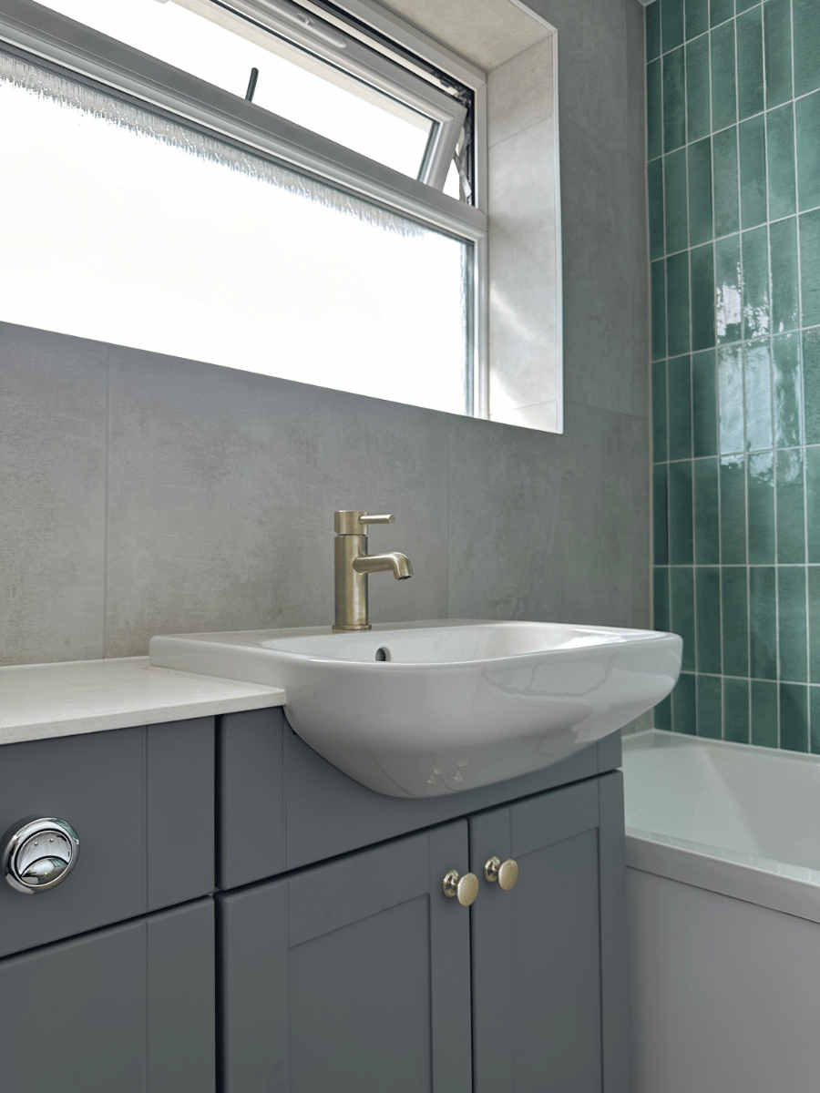 Full bathroom installation in Taunton featuring a grey vanity unit, white basin, brushed brass tap and green feature tiles, completed by Plumb Inc.
