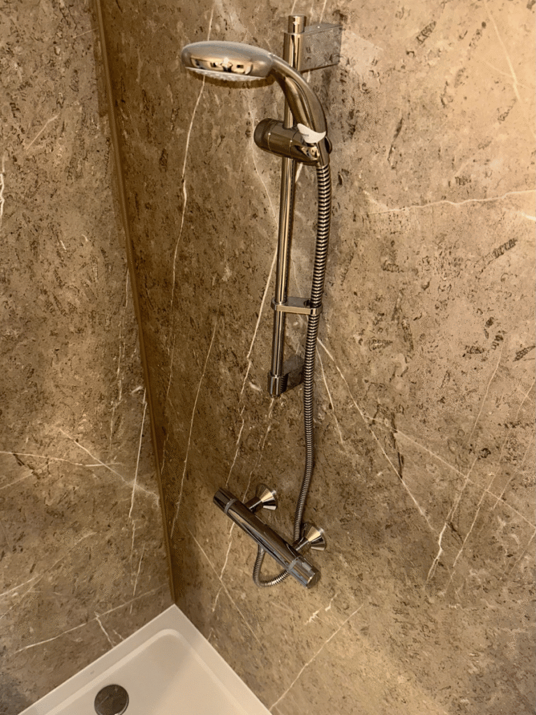 Chrome thermostatic shower installation with handheld shower head and stone-effect wall shower panels, completed by Plumb Inc in Taunton.